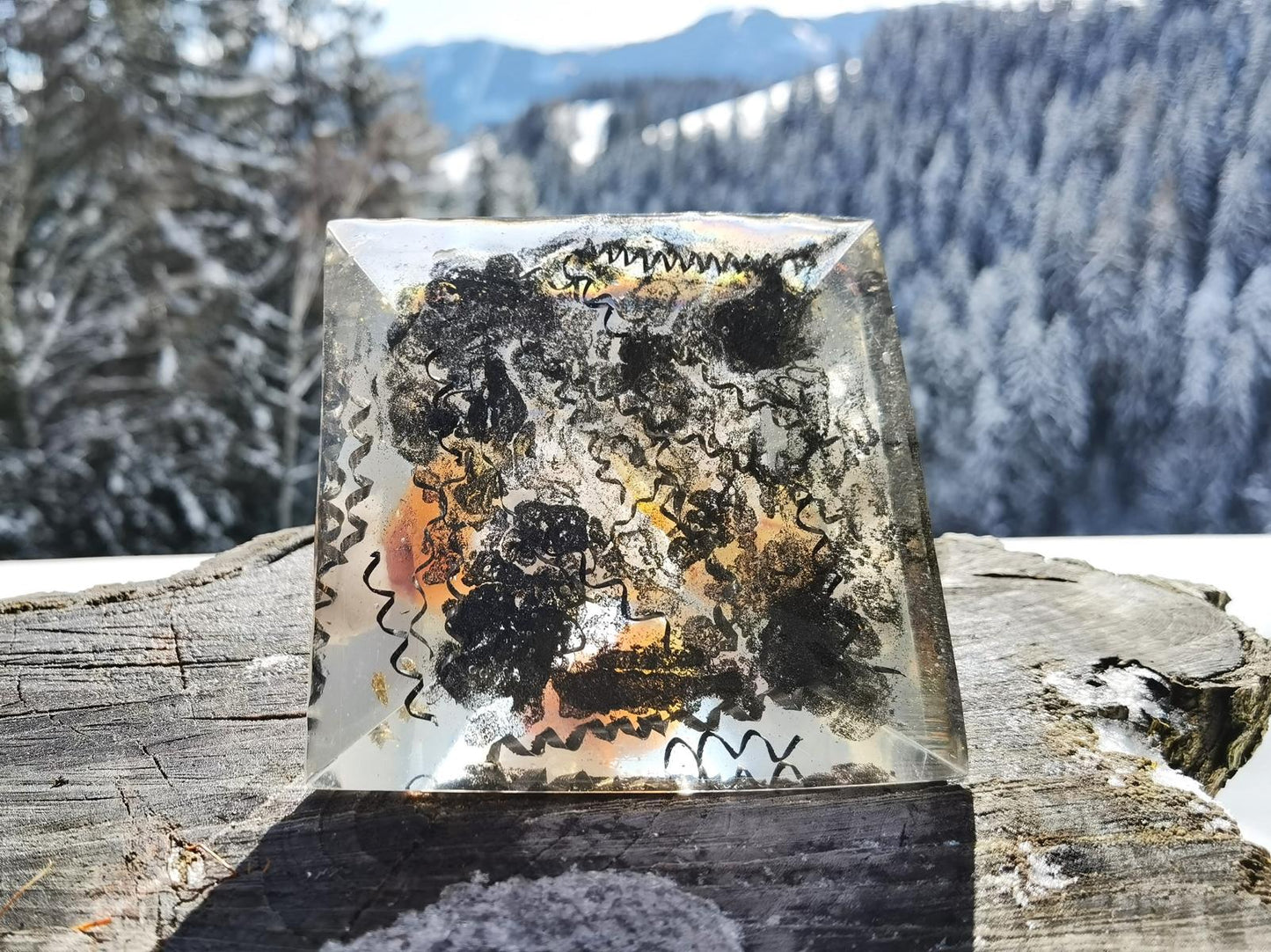 Basisansicht der Karneol-Flammenpyramide mit Schichten aus Metallspänen und Kristallen, umgeben von einer winterlichen Naturkulisse.