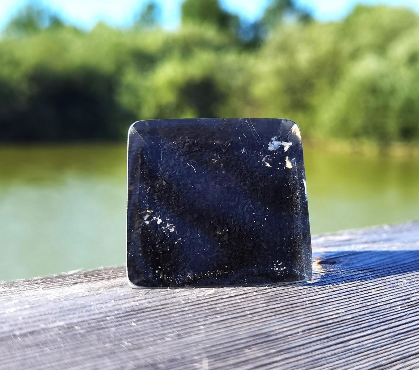 Mini-Orgon-Pyramide auf Holzoberfläche mit grünem Naturhintergrund.