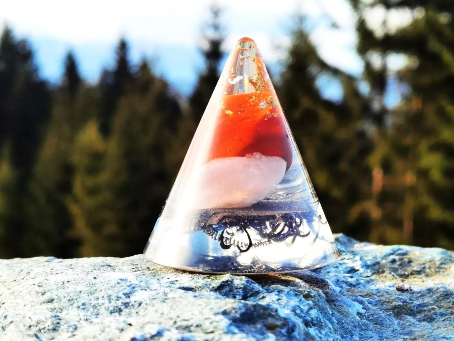 Handgefertigter Orgonit-Kegel mit rotem Jaspis, Rosenquarz und Bergkristall, perfekt für Erdung und Stabilität, dargestellt vor einem Waldhintergrund.