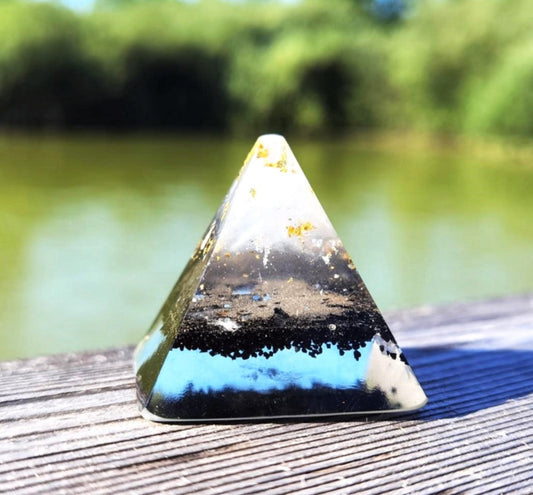 Seitenansicht einer Mini-Orgon-Pyramide mit Schungit und Gold vor einem natürlichen Hintergrund.